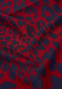 Tissu rouge avec motif léopard irrégulier bleu foncé, présenté avec des plis doux et un tissage texturé.