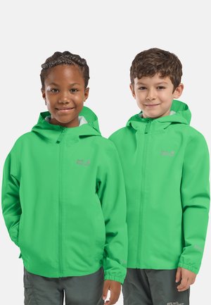 Twee kinderen die heldergroene gewatteerde jassen met capuchon dragen, staan naast elkaar en lachen tegen een effen achtergrond.