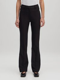 Schwarze ausgestellte Hose mit glatter Textur, ausgestattet mit einem Taillenbund, Gürtelschlaufen und einem gefalteten Vorderteil, kombiniert mit schwarzen, flachen Schuhen.