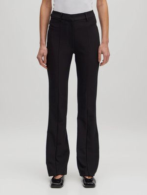 Zwarte flared broek met een gladde textuur, voorzien van een tailleband, riemlussen en een geplooide voorkant, gecombineerd met zwarte, platte schoenen.