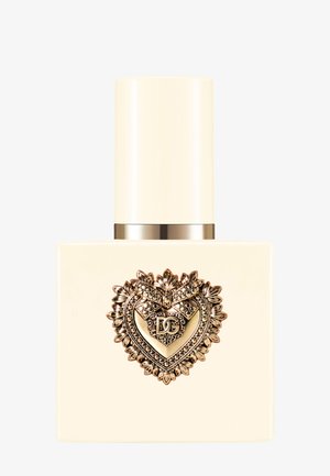 Flacon de parfum carré ivoire avec un emblème en forme de cœur doré et un bouchon, orné d'un nœud et des petites initiales DG au centre.