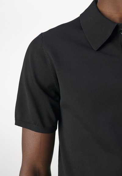 Svart polo-skjorte med klassisk krage, korte ermer og en glatt, lett tekstur. Har en knappelukking ved halsen.