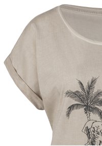 T-shirt beige à manches courtes avec un col rond, présentant un graphique de palmier noir et d'éléphant sur le devant. Tissu doux et texturé.