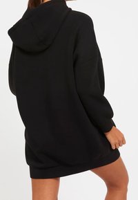 Svart oversized hoodie klänning med en stor huva, långa ärmar och ribbade mudd, tillverkad av mjukt material. Enkel, enfärgad utan mönster.