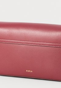 Maroon leather clutch purse with a textured surface, featuring a stitched line across the front and a gold "FURLA" logo. Smooth finish.