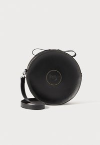 Black leather circular bag with yellow stitching. Adjustable strap and zipper closure. Logo embossed on front. Smooth texture.