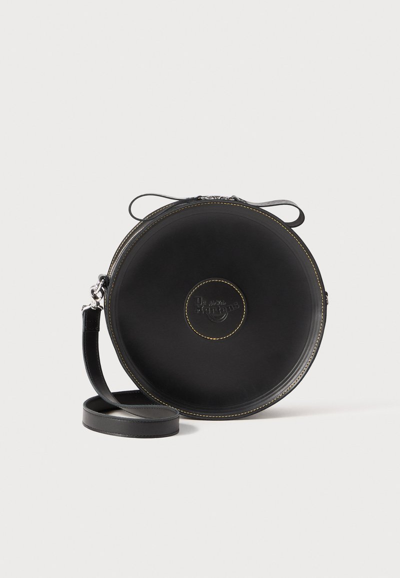 Black leather circular bag with yellow stitching. Adjustable strap and zipper closure. Logo embossed on front. Smooth texture.