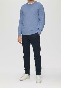 Niebieski sweter dziany z długim rękawem i okrągłym dekoltem, zestawiony z ciemnymi spodniami i białymi trampkami. Materiał o fakturze, luźny krój.