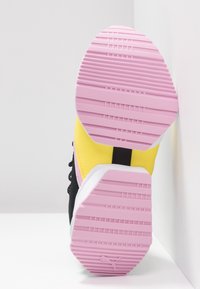 Semelle de basket rose avec grip texturé, montrant des parties supérieures noires, jaunes et blanches sur fond blanc.