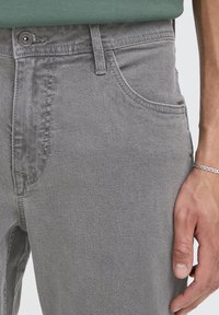 Jeans in denim grigio con una texture liscia, caratterizzati da un design classico a cinque tasche, chiusura con bottoni e leggere sfumature sul tessuto.