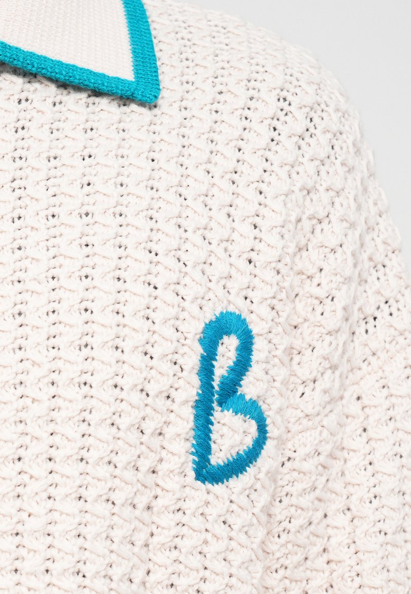 Knitted sweater in cream with a textured pattern, featuring a turquoise embroidered letter "B" and a contrasting collar.