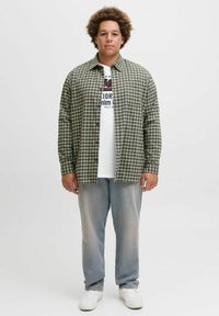 Grøn- og gråternet skjorte over en hvid grafisk t-shirt, parret med lysegrå jeans og hvide sneakers. Afslappet pasform og casual stil.