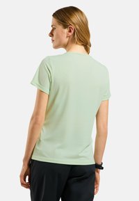 Light green athletic shirt with short sleeves, smooth texture, round neckline, and a relaxed fit, paired with dark pants.