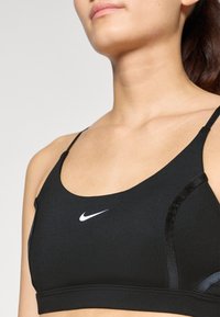Mustat urheiluliivit, jotka on valmistettu sileästä kankaasta, jossa on säädettävät hihnat ja pieni valkoinen Nike-logo edessä.