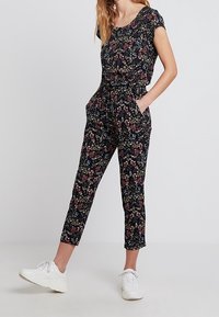 Blommig byxdress i svart tyg med korta ärmar, som har en smal passform, sidofickor och ett blommönster i nyanser av röd, blå och grön.