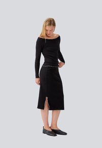 Haut en maille côtelée noire avec un col dégagé et des bords festonnés, associé à une jupe assortie de longueur genou avec une fente. Ballerines noires.