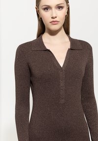 Brauner gerippter Strickpullover mit langen Ärmeln, Kragen und V-Ausschnitt. Mit dekorativen Knöpfen an der Vorderseite und einem subtilen metallischen Glanz.