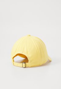 Gul bomulls baseball caps med justerbar metallrem på baksiden, vist på hvit bakgrunn.