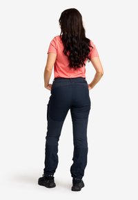 Kvinnlig utomhusoutfit: rosa kortärmad skjorta, marinblå stretchbyxor med fickor, elastisk midja, muddar och svarta vandringsskor.