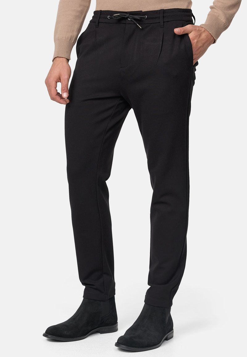 Pantalones negros ajustados con cintura elástica, con plisados y bolsillos laterales, combinados con botas negras hasta el tobillo. Textura de tela suave.