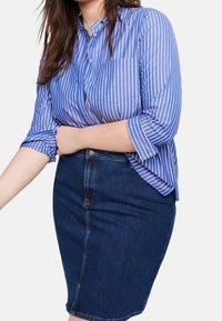 Camisa de botones a rayas azules y blancas con mangas remangadas, combinada con una falda lápiz de mezclilla oscura. Texturas suaves y diseño ajustado.