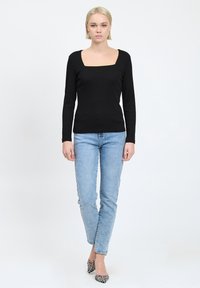 Maglia nera a maniche lunghe con scollatura quadrata, abbinata a jeans azzurri e tacchi a punta con motivo, su uno sfondo semplice.