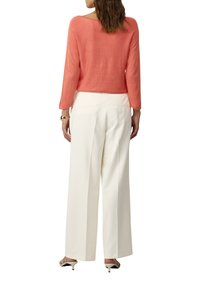 Koralowy sweter dzianinowy z rękawami o długości trzech ćwierć, połączony z białymi spodniami o szerokich nogawkach. Stylizacja charakteryzuje się luźnym krojem i miękką fakturą.