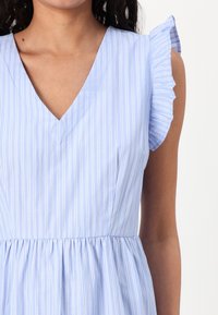 Hellblaues Kleid mit weißen vertikalen Streifen, V-Ausschnitt und Rüschenshcultern. Fließt sanft an der Taille mit gerafftem Stoffdetail.