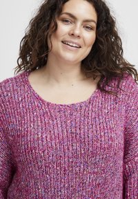 Stickad tröja i rosa nyanser med en texturerad, ribbad struktur. Har en bred rundad halsringning och långa ärmar.