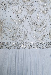 Robe bleu clair avec motifs de feuilles en sequins argentés et accents de perles. Corsage doux et texturé menant à une jupe en tulle plissée.