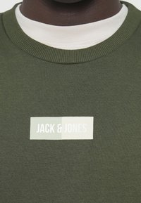 Zelená bavlnená mikina s rebrovaným výstrihom; obsahuje obdĺžnikový biely a svetlozelený logovú nálepku s nápisom "JACK & JONES."