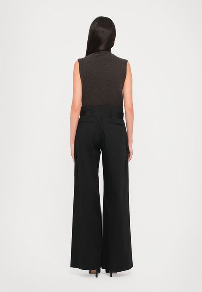 Black wide-leg trousers with a high waist, two side pockets, and a smooth fabric; paired with a fitted brown sleeveless top.