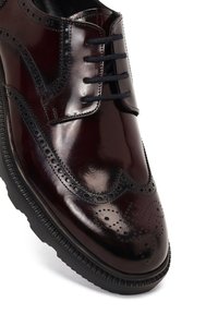 Zapato de vestir de cuero burdeos con un acabado brillante, que presenta detalles de brogue perforados, cordones y una suela de goma negra texturizada.