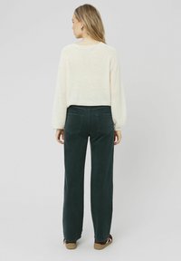 Pull en tricot ivoire pour femmes avec des manches ballon, associé à un pantalon large en velours côtelé vert foncé et des baskets marron, vu de dos.