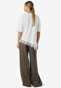 Hvit t-skjorte med korte ermer og blonderkant nederst. Plagget er kombinert med brune bukser med vide ben.