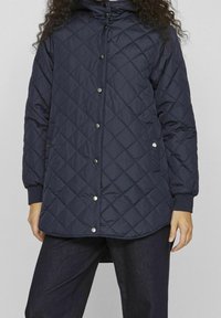 Granatowa pikowana kurtka ocieplana z kapturem, zatrzaskami i ściągaczami przy mankietach, o długości do połowy ciała, z kieszeniami po bokach.