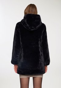 Cappotto in ecopelliccia nera con cappuccio, maniche lunghe e una consistenza morbida. Il design è lungo fino al ginocchio con una vestibilità comoda, privo di hardware visibile.