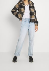 Fleece zip-up jacket in black and tan plaid, paired with light blue straight-leg jeans. Black shoes with a textured surface and detail on the toes.