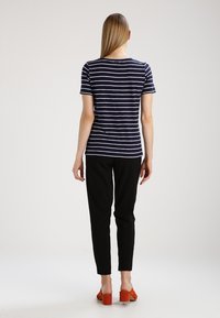 Camisa de rayas en azul marino y blanco de manga corta combinada con pantalones ajustados negros y zapatos de tacón bloque naranja. Tejido suave, corte relajado.