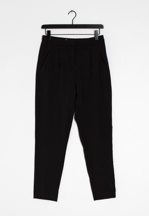 Zwarte op maat gemaakte broek met voorplooien en zijzakken, hangend aan een zwarte klemhanger tegen een witte achtergrond.