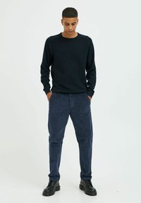 Navy crewneck-tröja i texturerat material, kombinerad med marinblå corduroybyxor. Svarta snörboots fulländar outfiten.