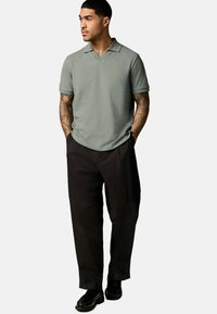 Kortærmet, lysegrøn polo t-shirt med en notch krave, parret med løse, sorte bukser og sorte sko. Glat tekstur, afslappet design.