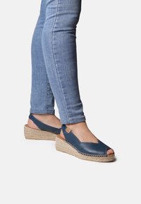 Blue leather wedge sandals with open-toe design, natural woven jute sole, and ankle strap; smooth texture with stitching accents.