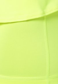 Tela de un brillante amarillo neón con una textura estriada. Presenta costuras y juntas visibles, creando un diseño ajustado adecuado para ropa deportiva.