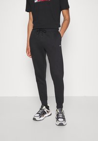 Svarta joggers med dragsko i midjan, kombinerat med en svart T-shirt med en röd logotyp, samt sportskor med flerfärgade detaljer.