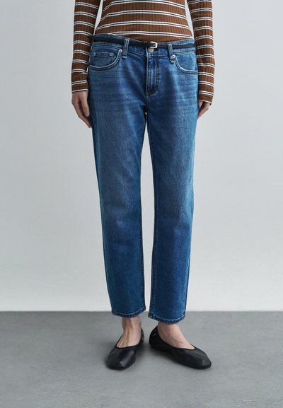 Blaue Jeans aus Denim mit geradem Schnitt, Fünf-Taschen-Design und gesteppten Details. Kombiniert mit schwarzen flachen Schuhen und einem braun gestreiften Oberteil.