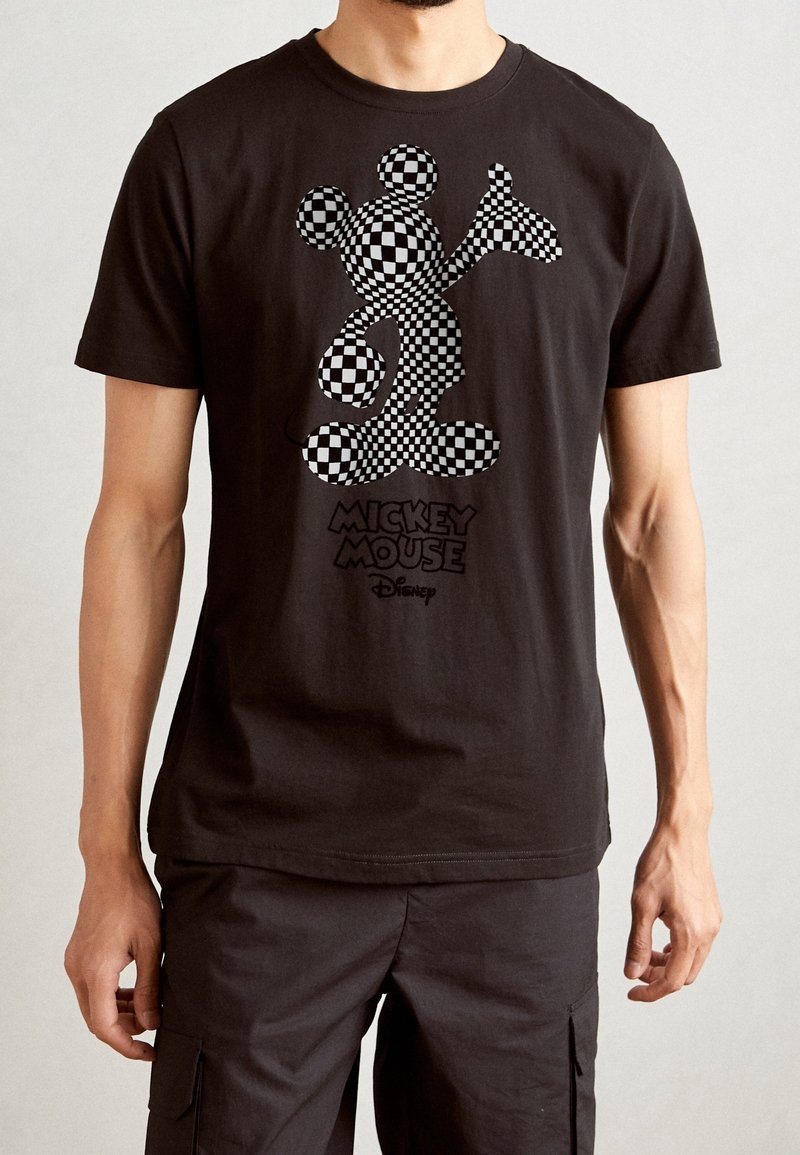 Černé bavlněné tričko s potiskem Mickey Mouse v kostkovaném vzoru a textem "Mickey Mouse" pod ním. Krátké rukávy a kulatý výstřih.