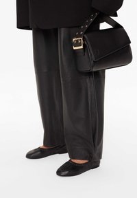 Czarna skórzana torba złożoną klapą, złote okucia, zestawiona z luźnymi czarnymi skórzanymi spodniami oraz czarnymi, płaskimi butami wsuwanymi z marszczonymi krawędziami.