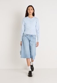 Ανοιχτό μπλε ζακέτα με ραβδωτή υφή και κουμπιά, σε συνδυασμό με ανοιχτό μπλε denim culottes. Μαύρα παπούτσια και λευκά καλσόν ολοκληρώνουν το ντύσιμο.