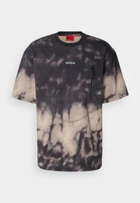 Camiseta de manga corta en un patrón de tie-dye negro y beige; cuenta con un bolsillo con cremallera en el lado izquierdo del pecho y detalle cosido en el dobladillo. Logo de HUGO visible.
